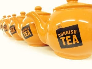 A row of six orange teapots from Cornish Tea.