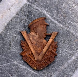 Rusted metal badge depicting a profile of Winston Churchill and a Victory V in the foreground
