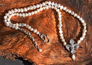 A silver fleur de lis pendant on a necklace of pearls