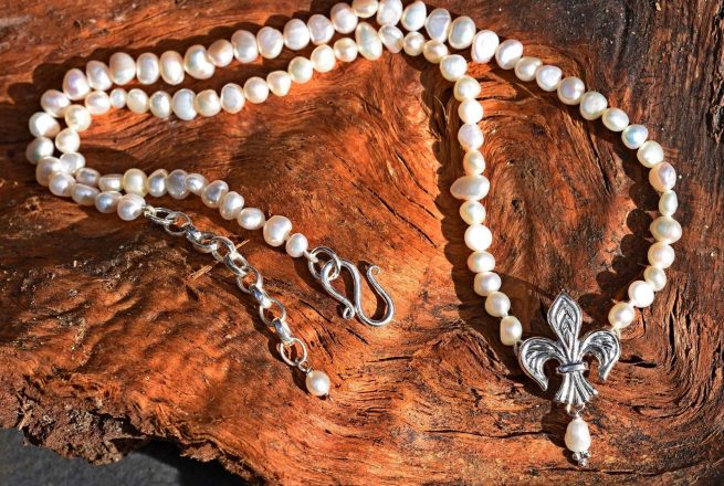 A silver fleur de lis pendant on a necklace of pearls by Mallards.