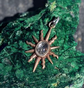 A bronze sunburst pendant by Mallards with a blue stone centre