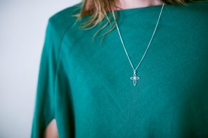 A sterling silver twist cross pendant by Mallards, worn on a chain against a jade-green top